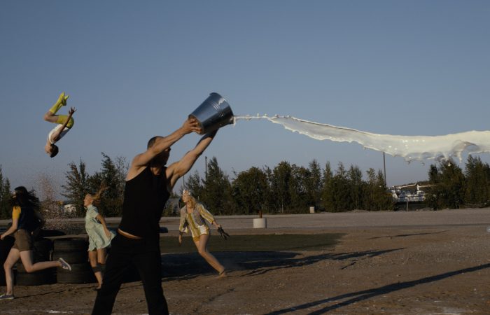 Man throwing bucket of milk with people running and jumping in the background
